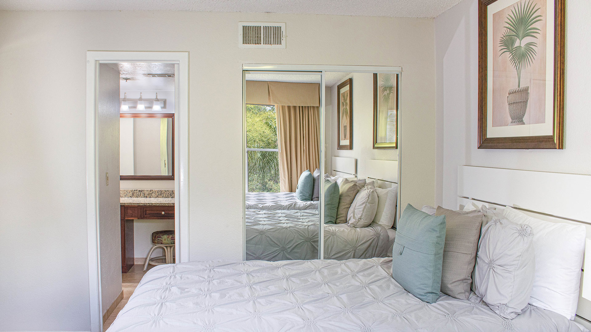 A wide view of a hotel room with a bed, mirror, and artwork.