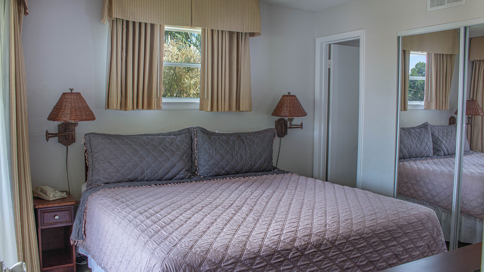 A neatly made bed with two nightstands and lamps in a simply furnished room with a window and mirror
