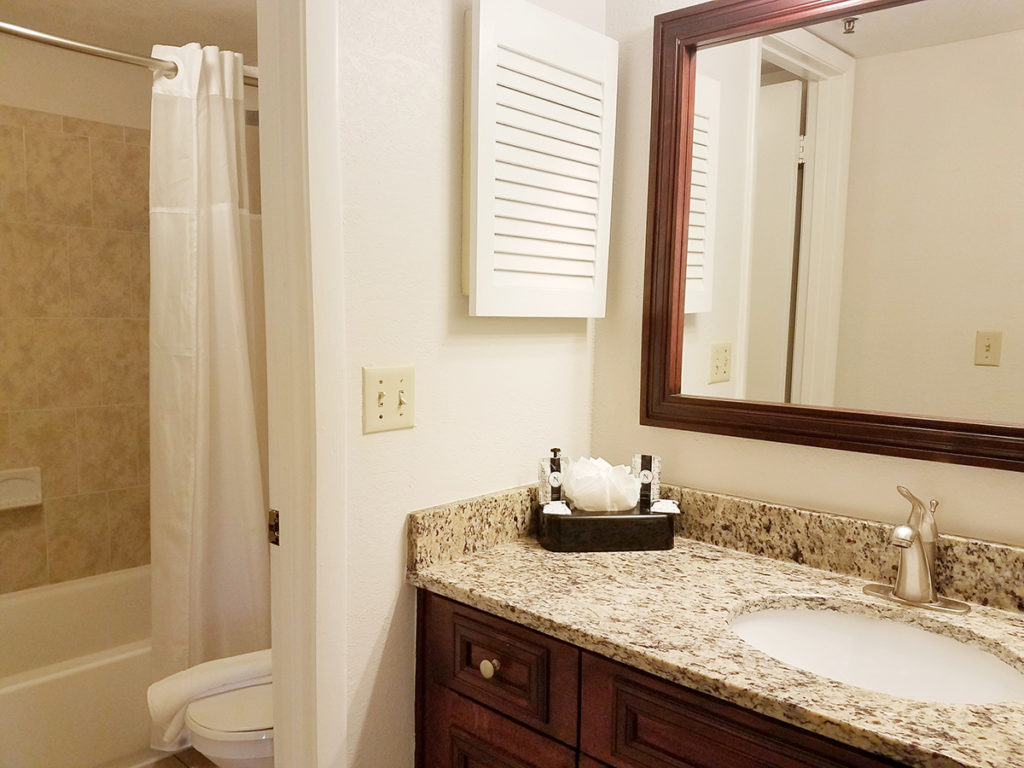 A clean and well-appointed bathroom with a granite countertop, dark wood cabinets, and a large mirror.