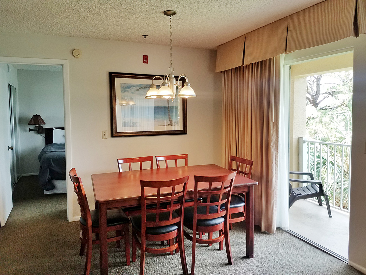 A dining area with a table and chairs, a balcony with a view, and a picture on the wall.