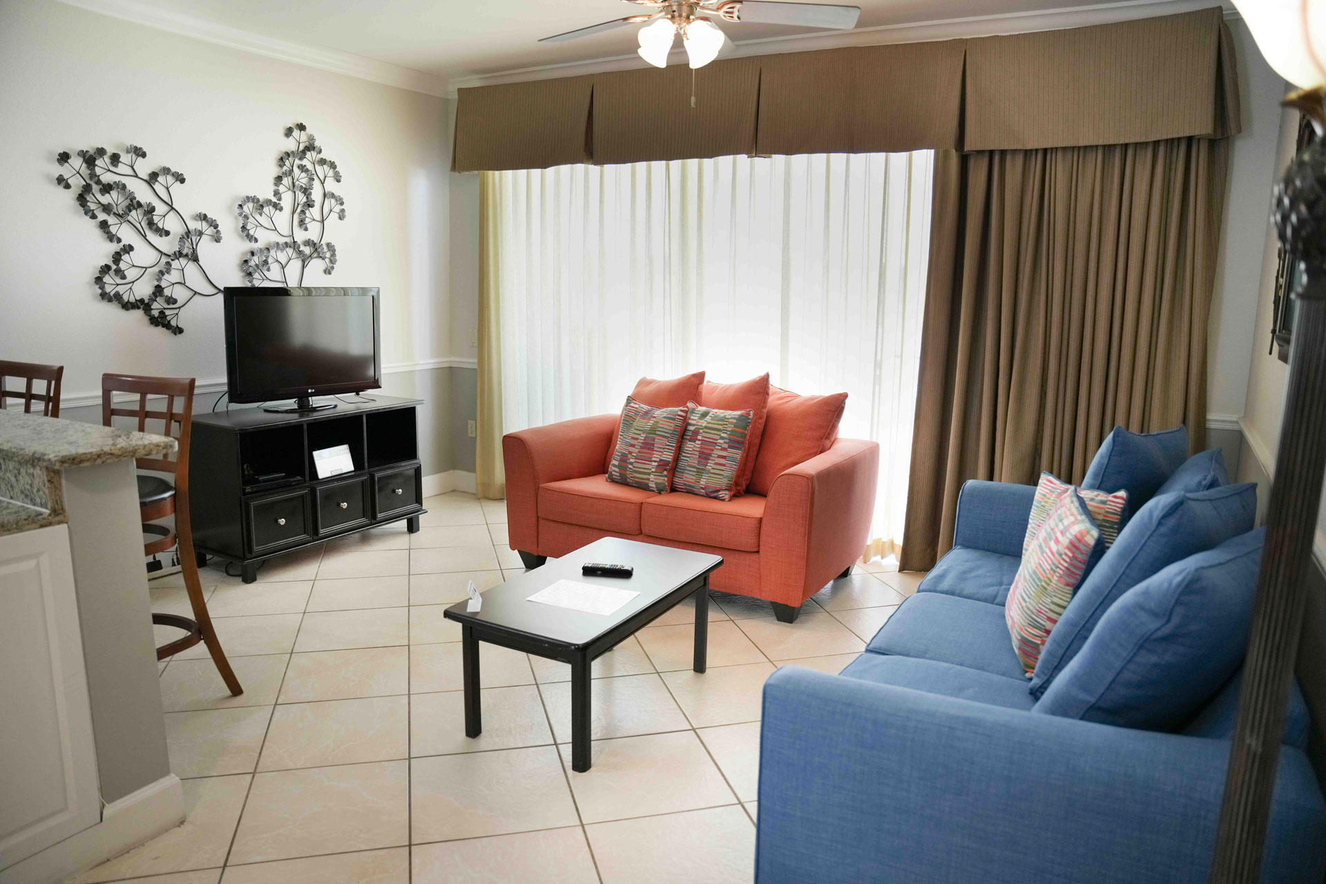 A wide view of a living room with a blue sofa, orange armchair, TV on a stand, and a coffee table.