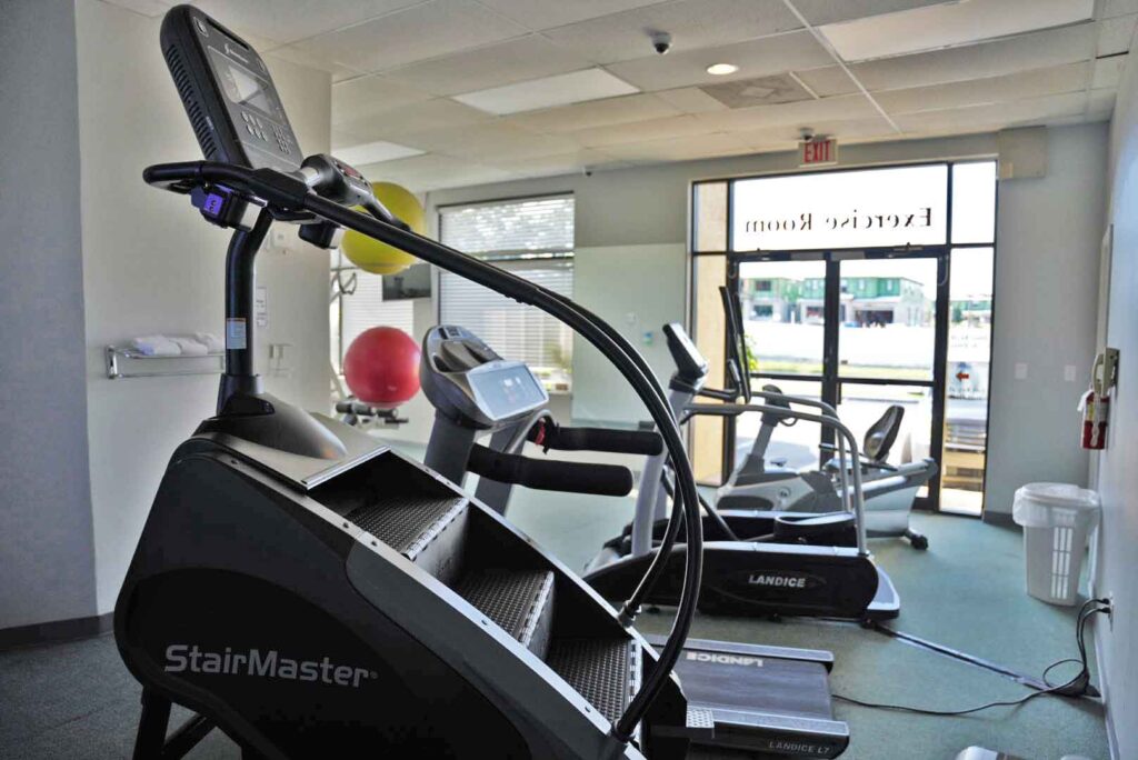 A gym with exercise equipment including a StairMaster, treadmill, and elliptical trainer.