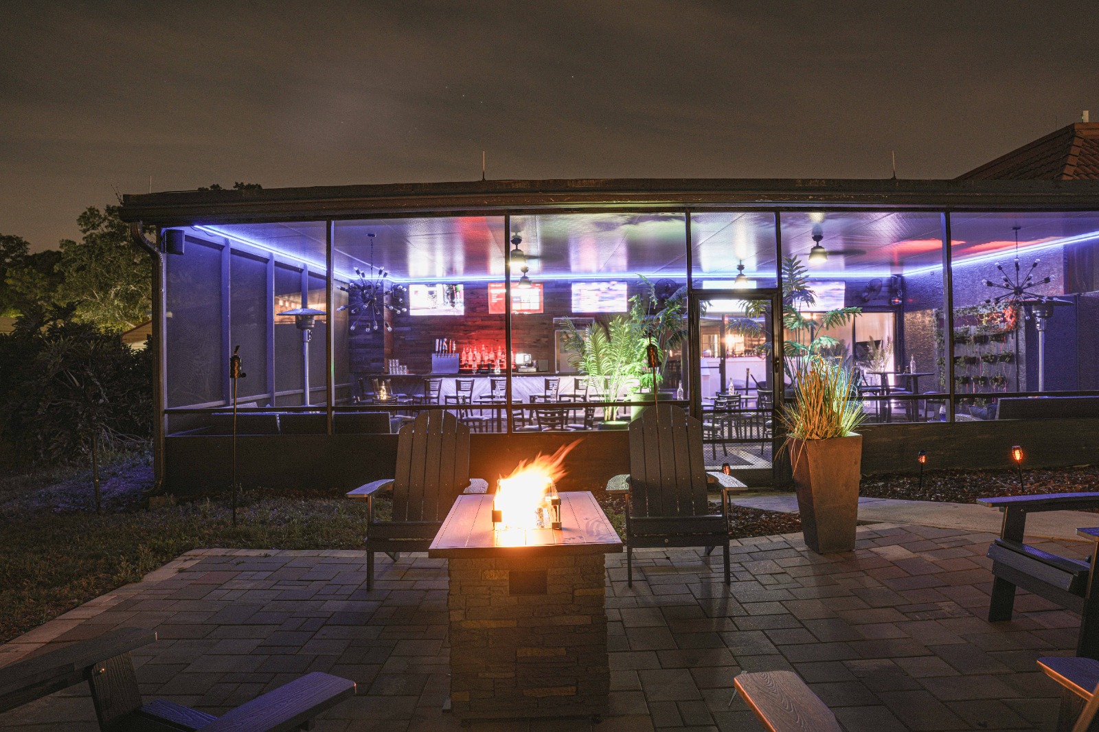 A glass-enclosed patio area with a fire pit and seating at night.